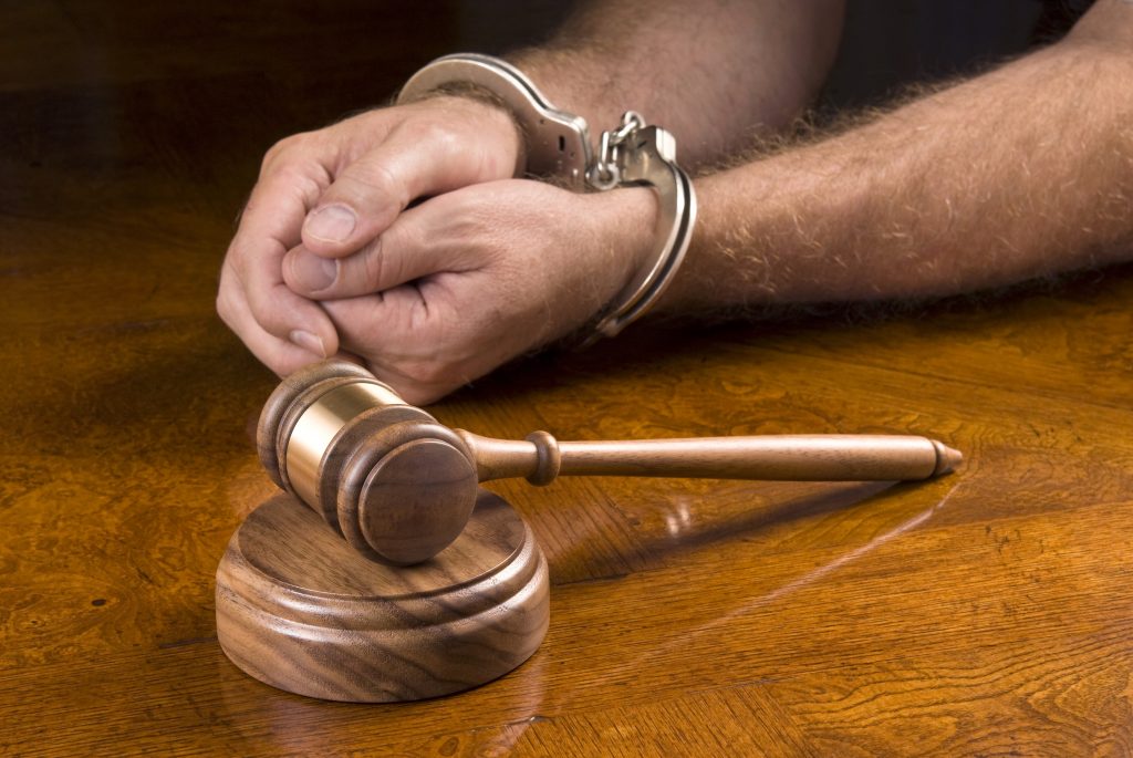 Photo of shackled hands next to a hammer and gavel