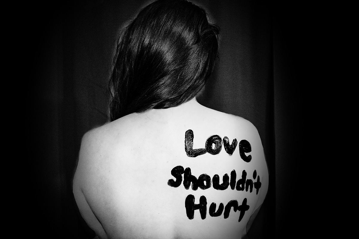 A black and white photo of a woman's bare back with words 'Love' in paint