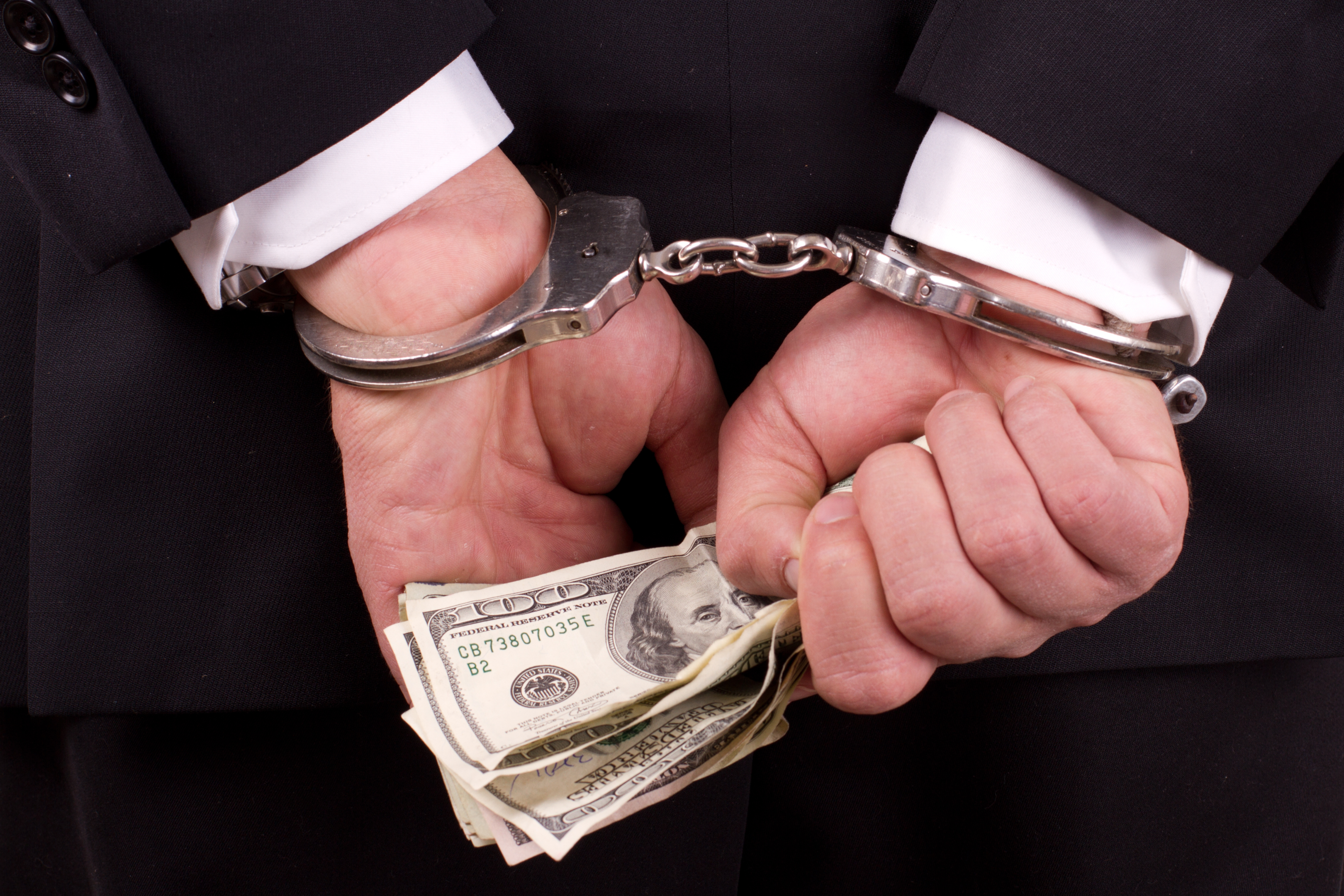 business man in handcuffs with hundred dollar bills in hand - Chicago Criminal Defense Attorney