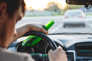dui criminal attorney Driver holding a beer bottle behind the wheel – illustrating DUI charges and legal defense provided by The Law Office of Purav Bhatt in Chicago.