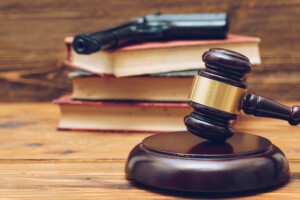 Judge gavel, law books and gun on a wooden background Judge gavel, law books and gun on a wooden background